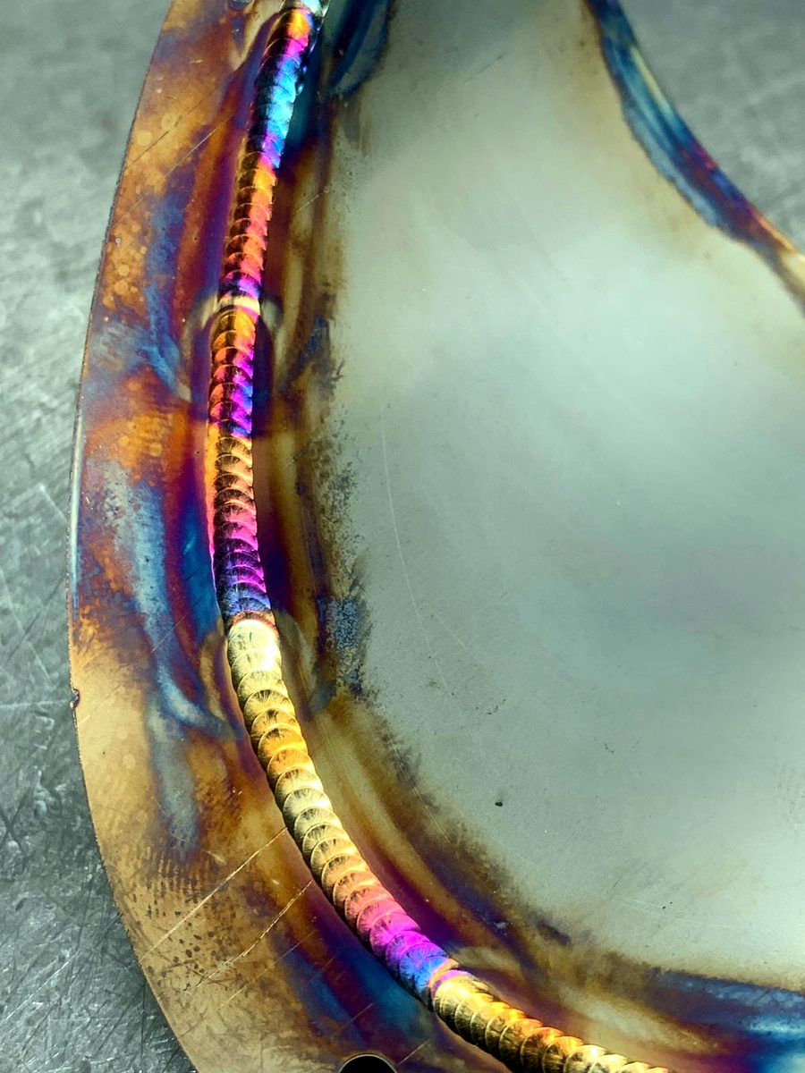 Close-up of a stainless steel TIG weld showing rainbow heat-tint colours